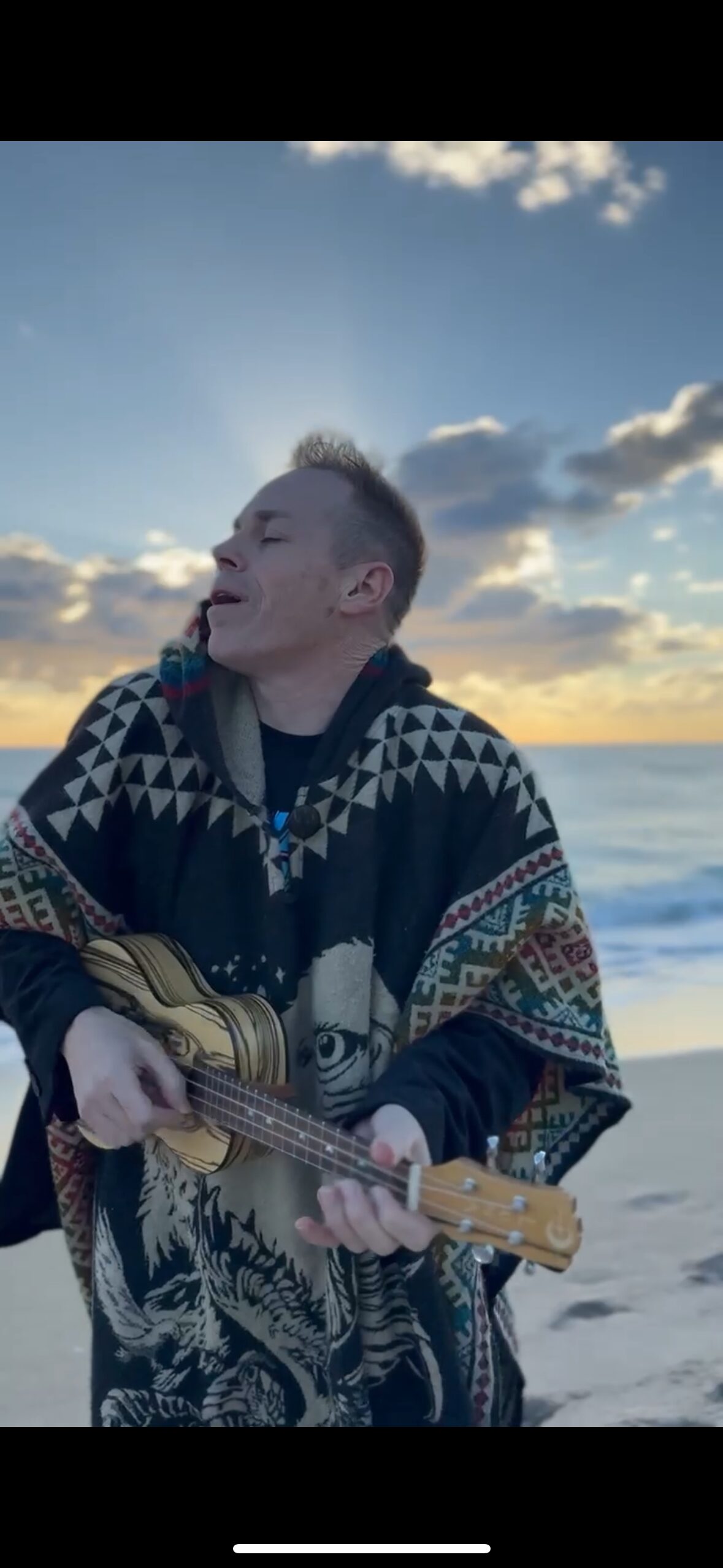 A solitary figure on a beach at sunrise with a ukulele, singing toward the water.
